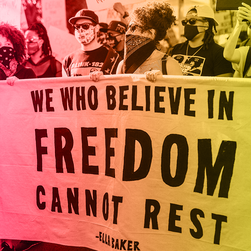 People marching hold a banner quoting Ella Baker. It says, 